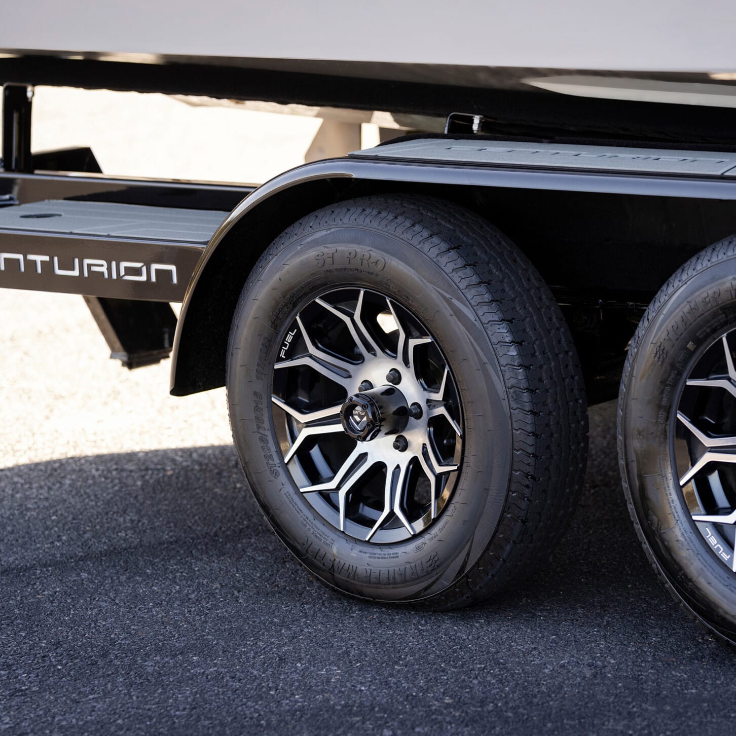 Close-up of a Centurion boat trailer showing two black wheels with silver rims on a paved surface.