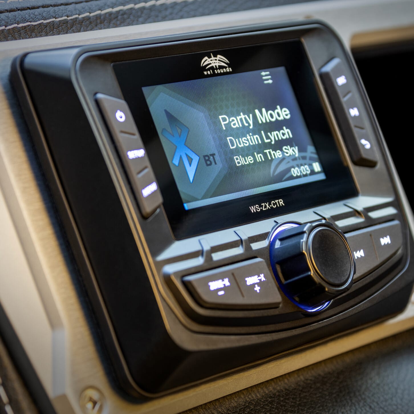 Close-up of a car stereo display showing music playing: 