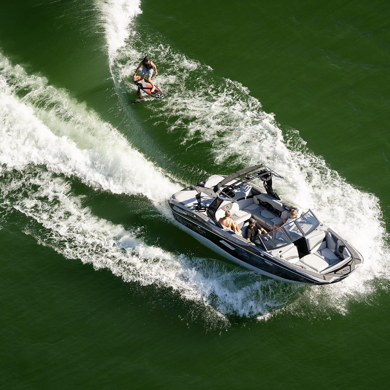 Aerial view of a motorboat towing a person on a wakeboard across green water.