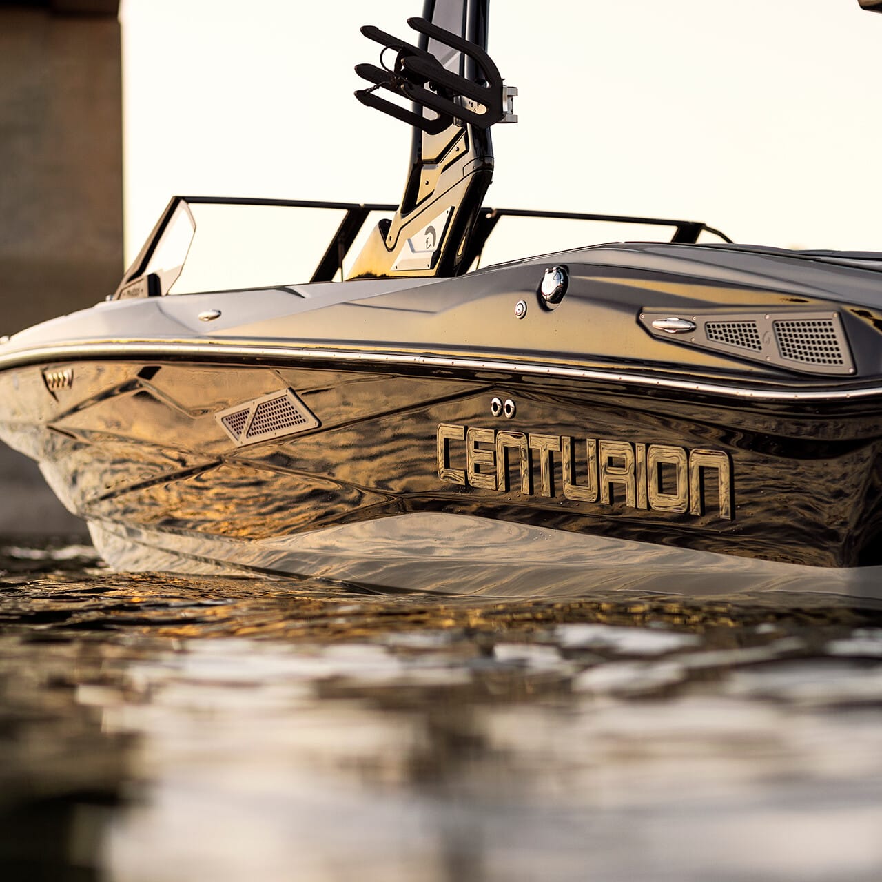 Close-up of a Centurion boat on the water near a bridge, reflecting the setting sun.