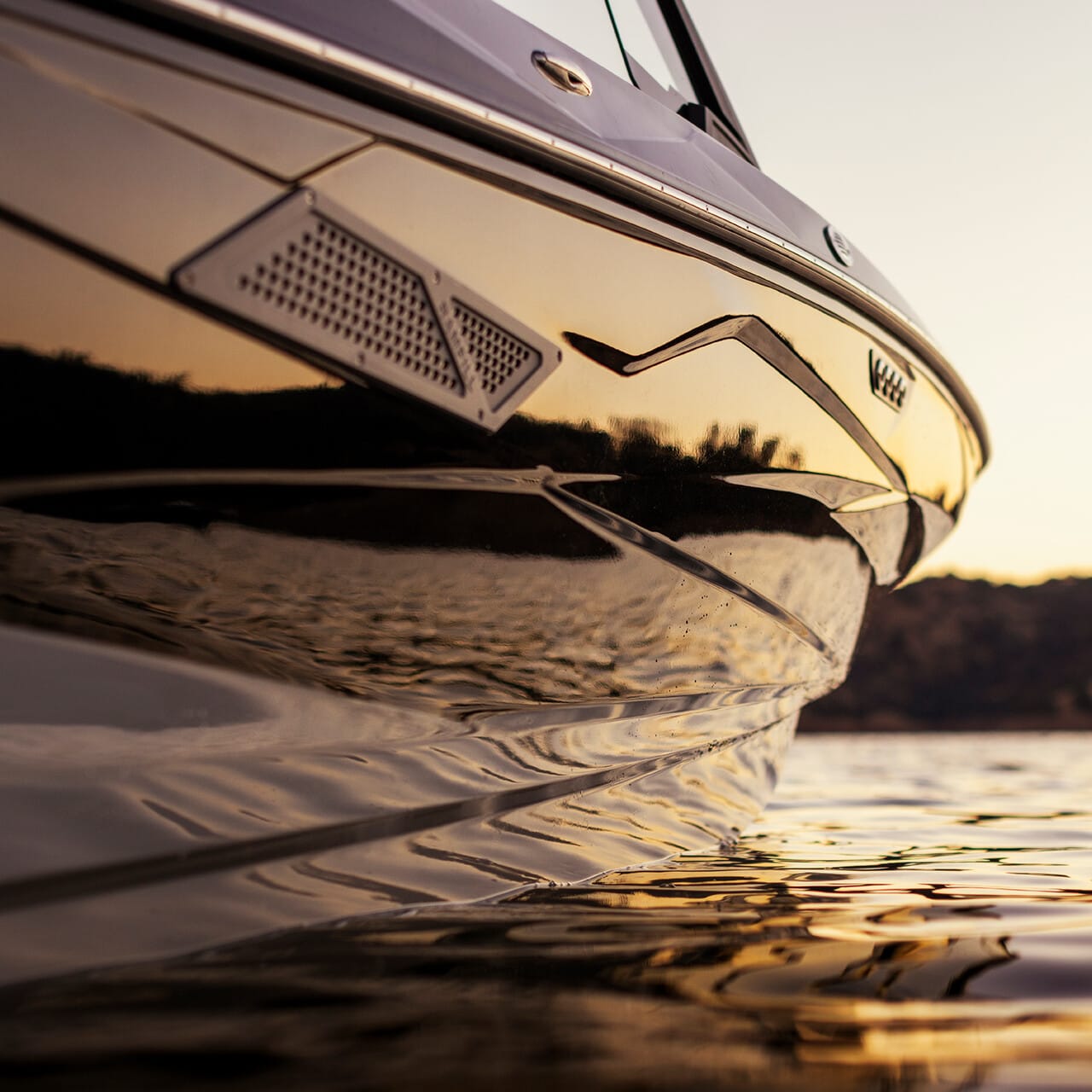 Close-up of a boat's side with reflective water at sunset, highlighting sleek lines and a calm seascape.