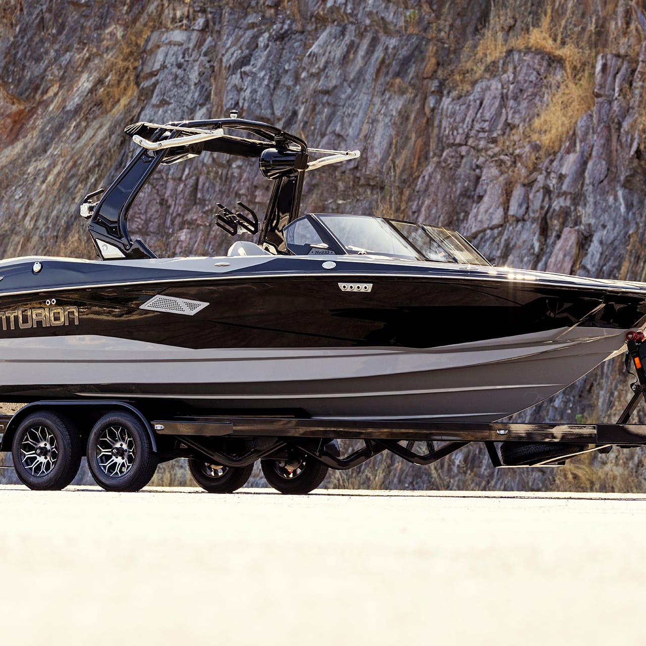 A black and gray Centurion boat on a trailer parked by a rocky hillside.