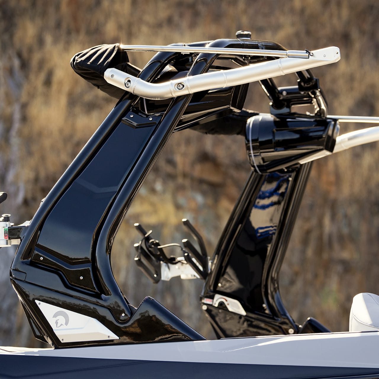 A close-up of two sleek black wakeboard towers on a boat, set against a rocky background.