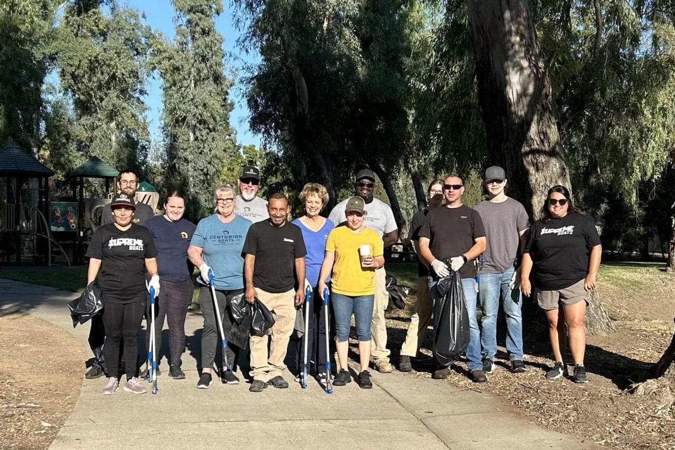 A group of people stand on a park pathway surrounded by trees, holding trash bags.