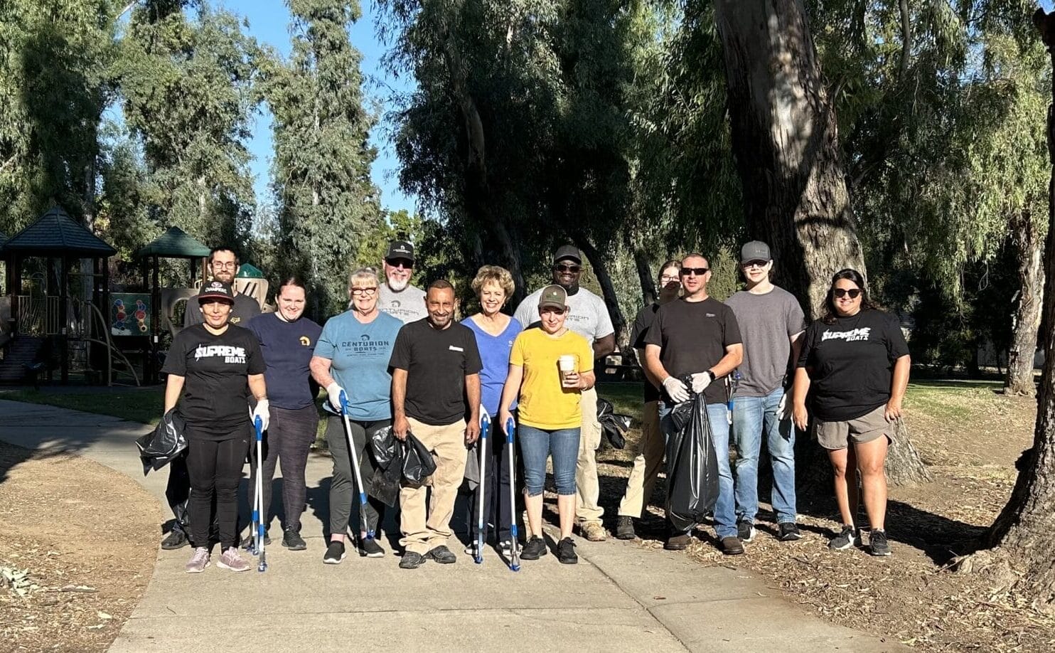 A group of people stand on a park pathway surrounded by trees, holding trash bags.