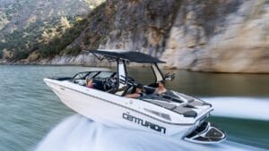 A white Centurion speedboat with four people aboard speeds across the water, with mountains visible in the background.