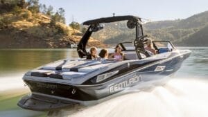 A speedboat with four people onboard moves swiftly across a lake surrounded by hills.