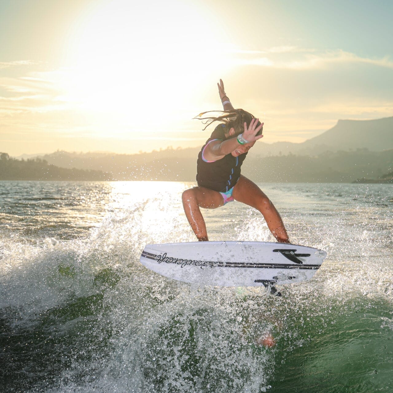 Person surfing on a wave during sunset, with water splashing around and mountains in the background.