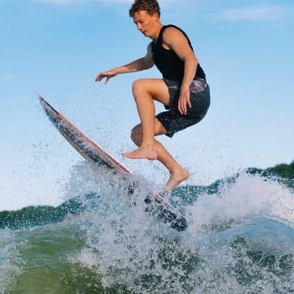 A person in a wetsuit is surfing, airborne above a wave, under a clear blue sky.