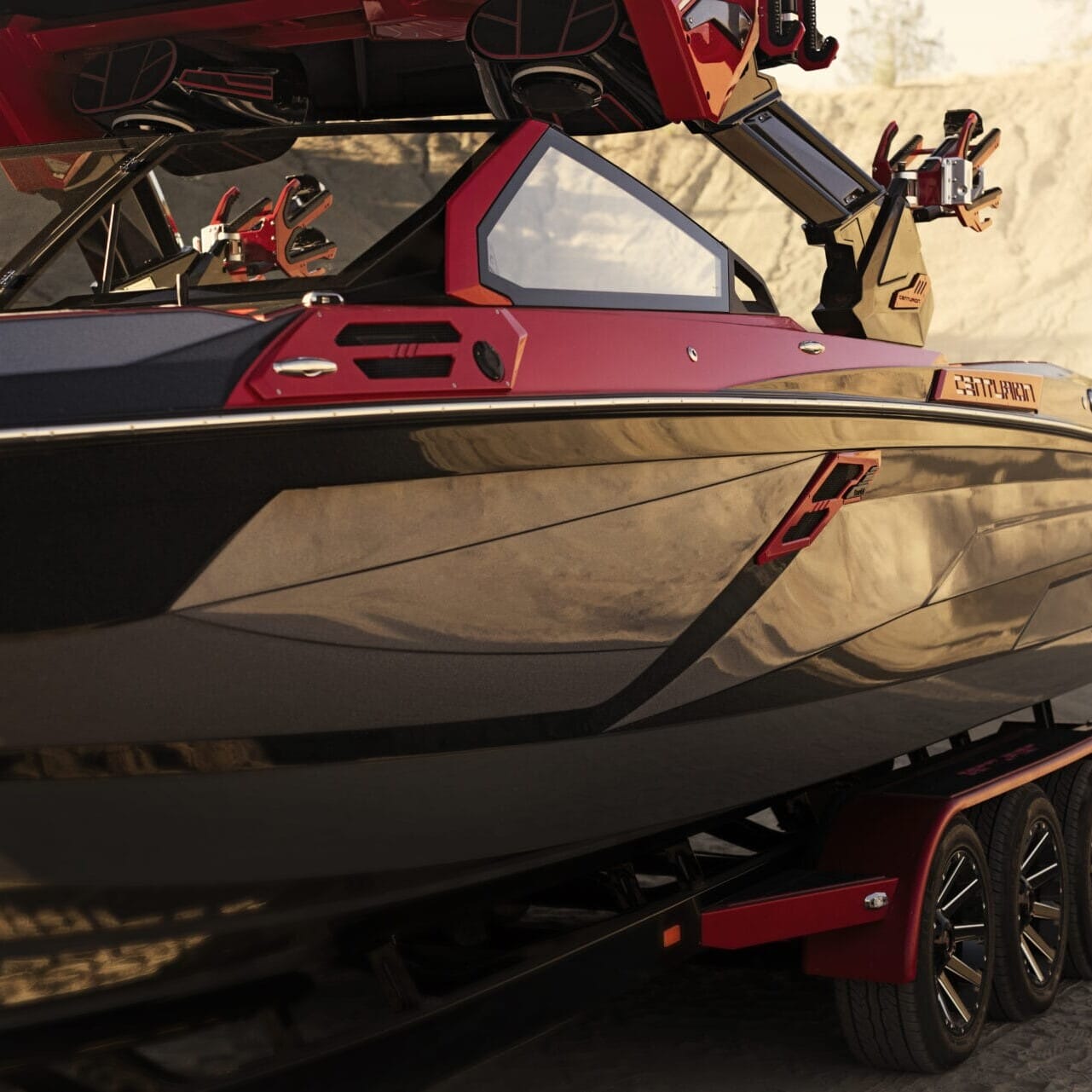 Close-up of a sleek, black and red boat featuring the Centurion Opti-V Hull design on a trailer, set against a sandy outdoor environment.