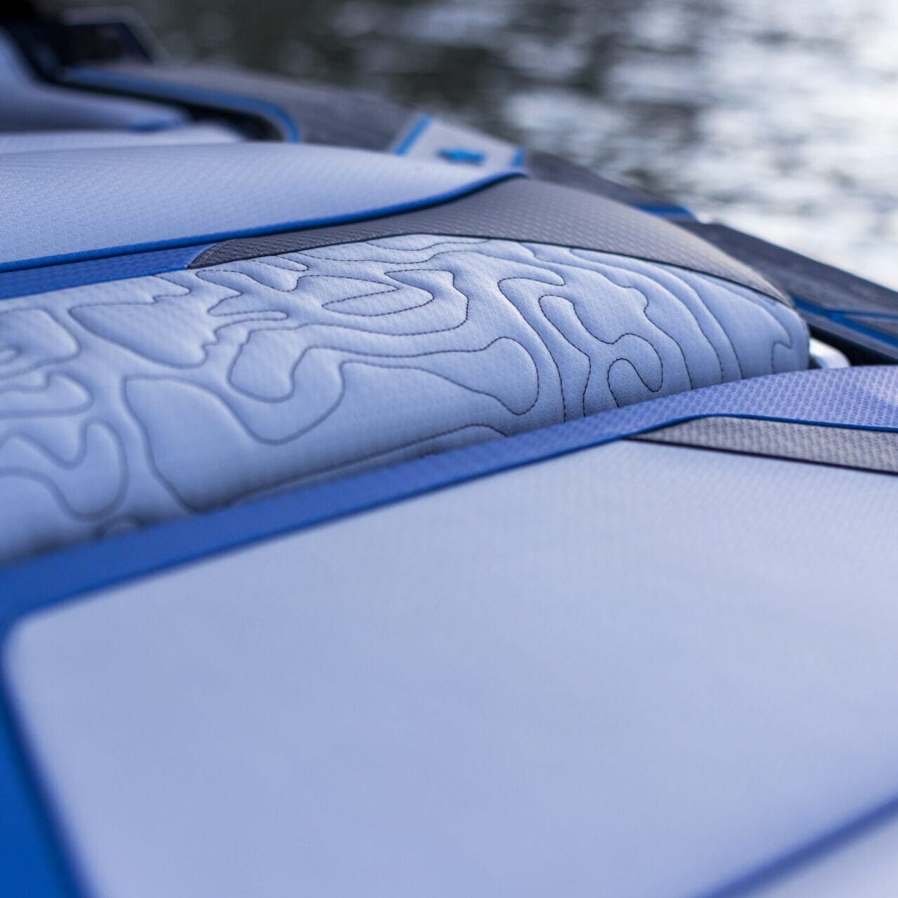 Close-up of a blue and white boat seat with textured patterns, reflecting the sleek design ethos of Centurion Opti-V Hull, set against a blurred water background.