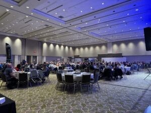 A large conference room with round tables, each occupied by multiple people engaged in discussions.