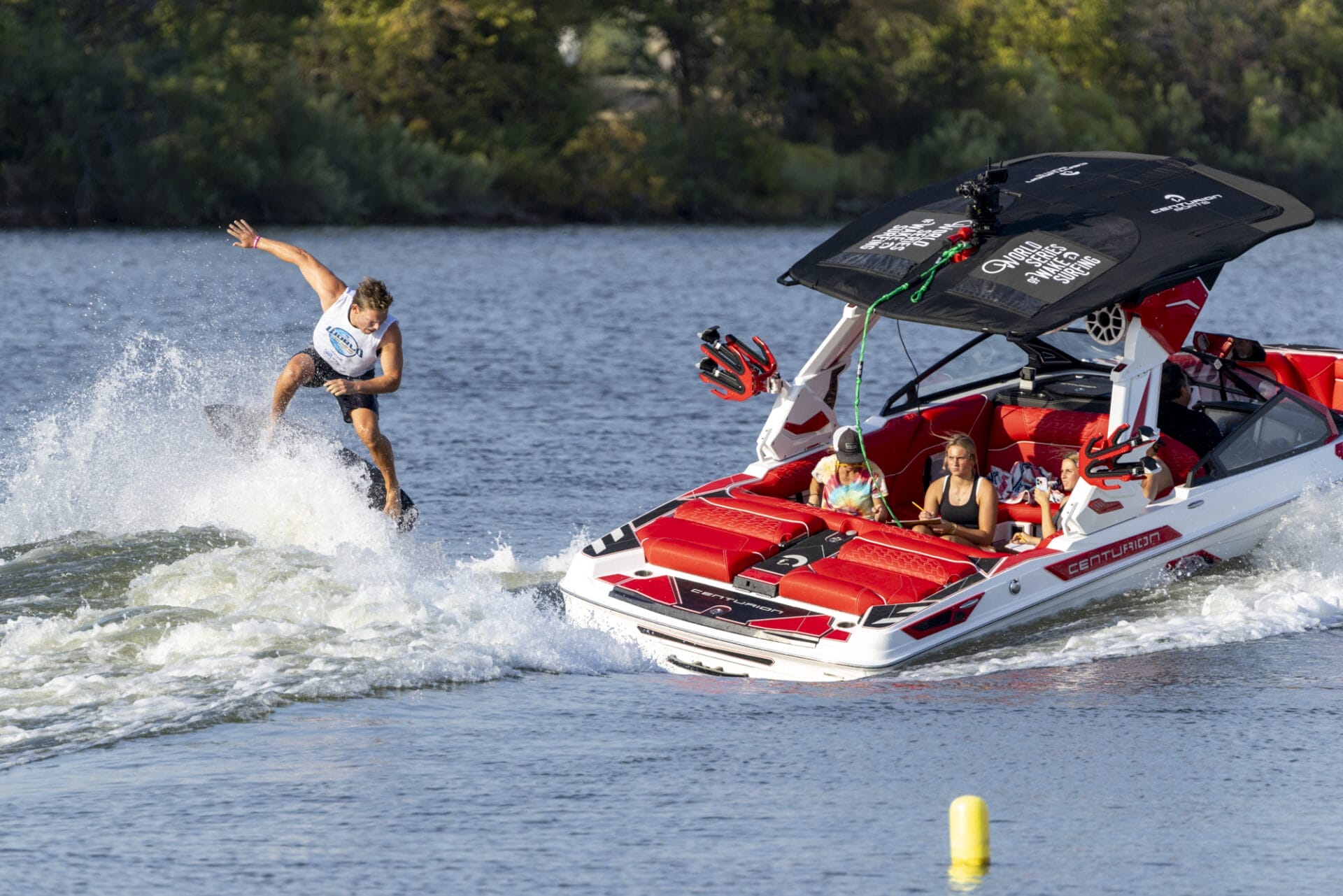 A person wakeboarding on a lake near a motorboat with passengers observing.