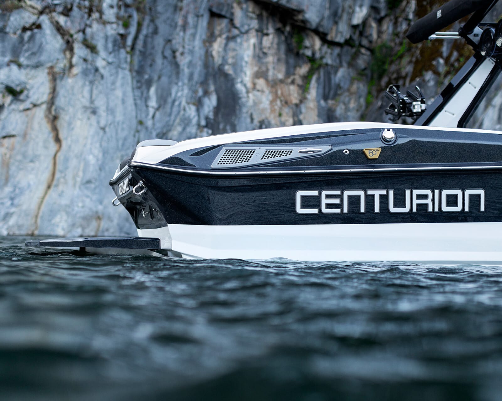Close-up view of the side of a Centurion Nv213 boat on water, with a rocky cliff face in the background.